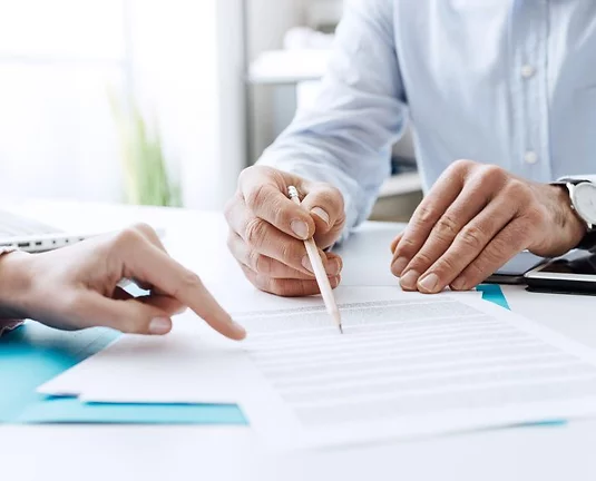 A set of hands going over a contract with a pencil and another hand pointing at the contract.