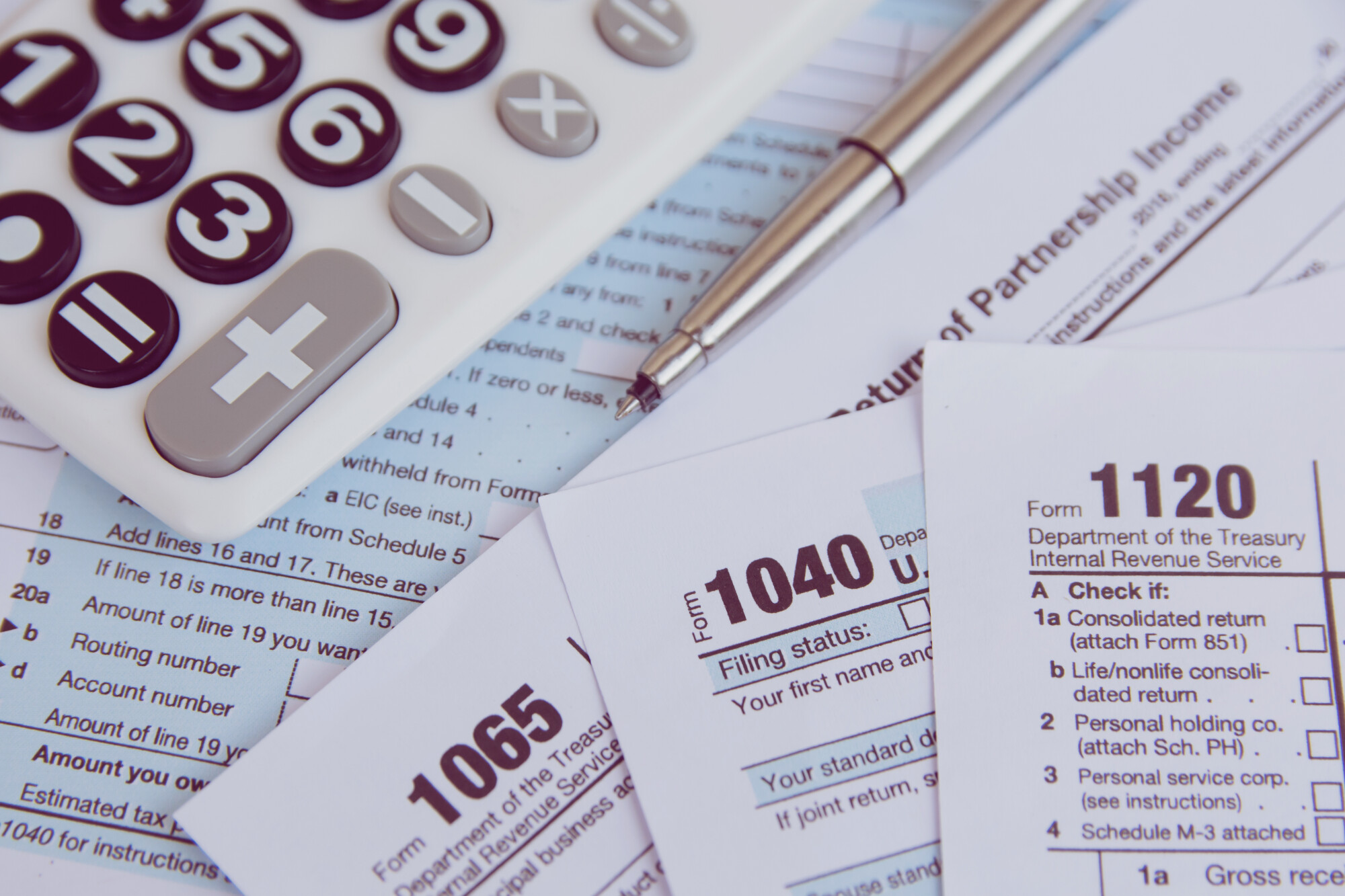 Various tax forms stacked on top of each other with pen and calculator above them.