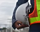 Close-up of a construction worker holding a white hard hat while wearing a reflective safety vest.