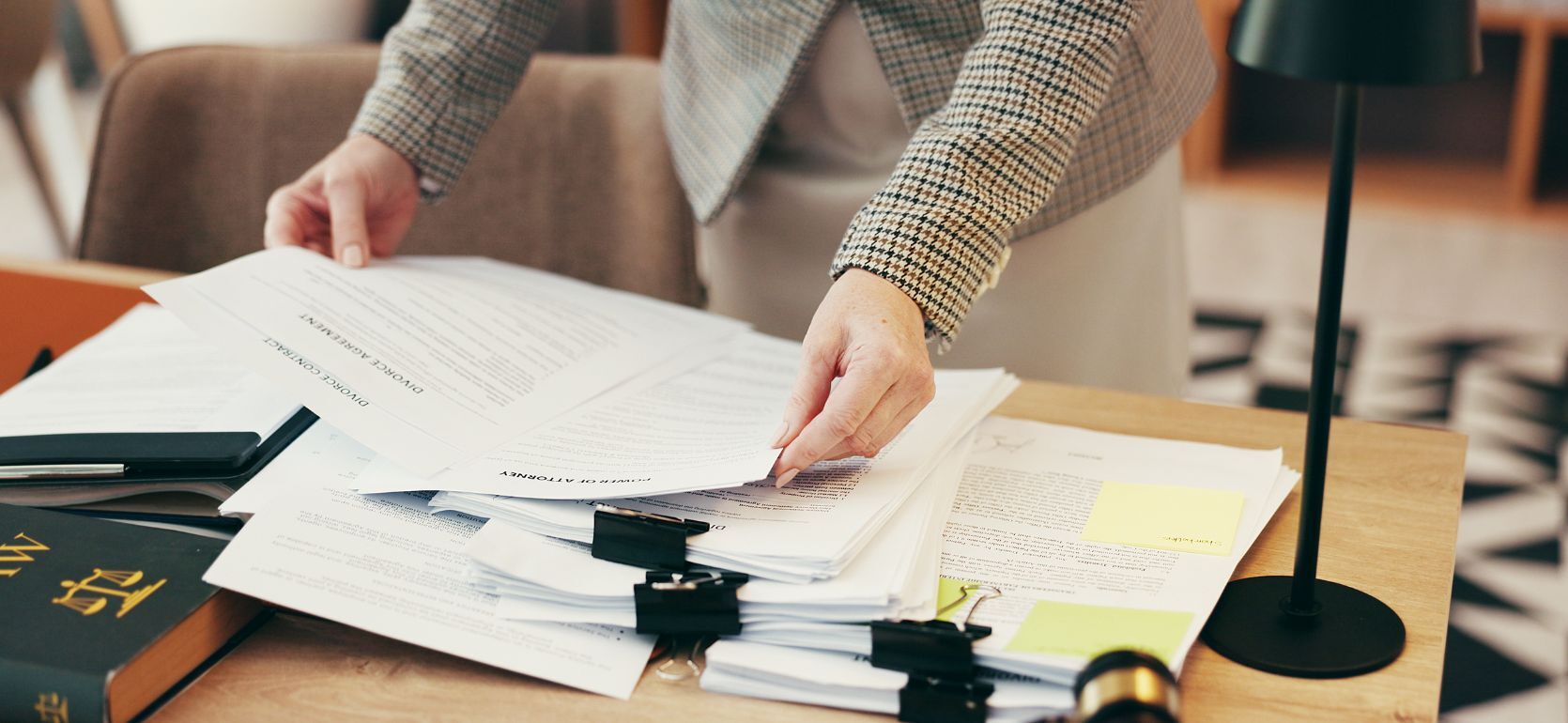 Woman looking over a pile of papers on a desk with a law book in the corner.
