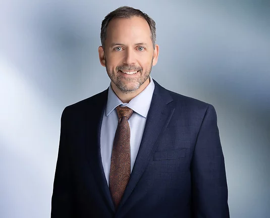 Man wearing blue sports coat with brown patterned tie smiles at camera