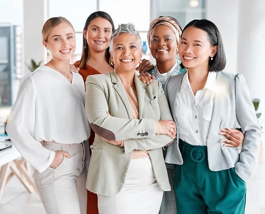 A group of 5 women wearing business attire and smiling at the viwer.