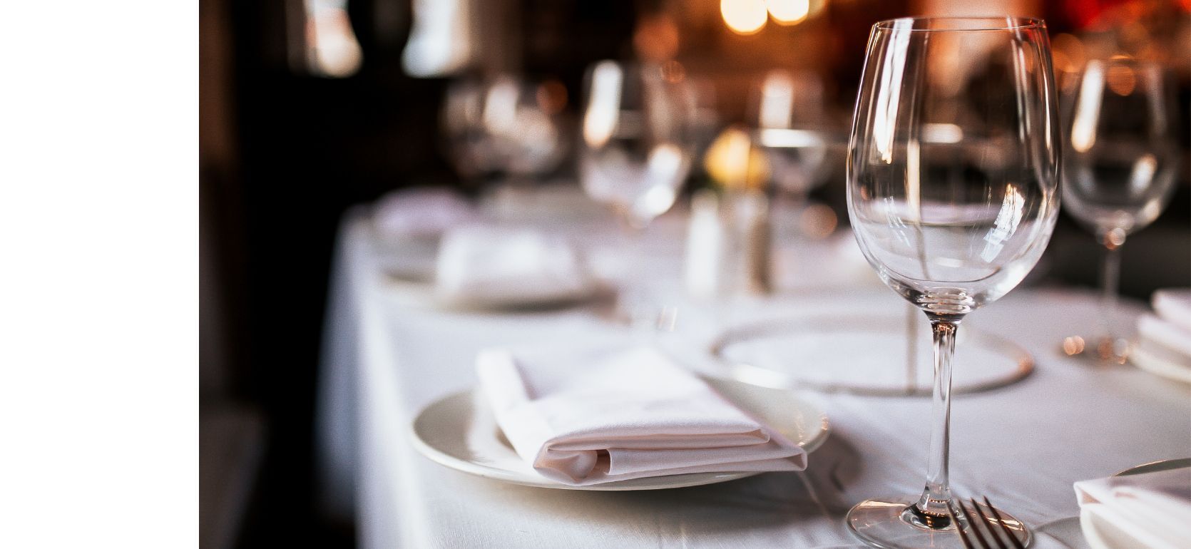 A wine glass and plate sitting on a white clothed table.