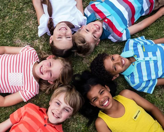 6 kids laying in a circle on the grass smiling at the camera.