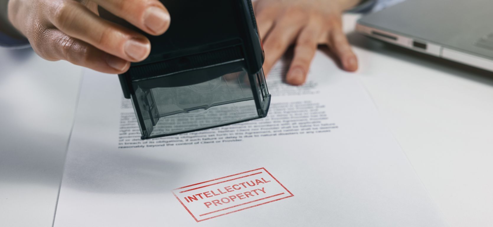 Someone stamping a paper that says "Intellectual Property" in red ink.
