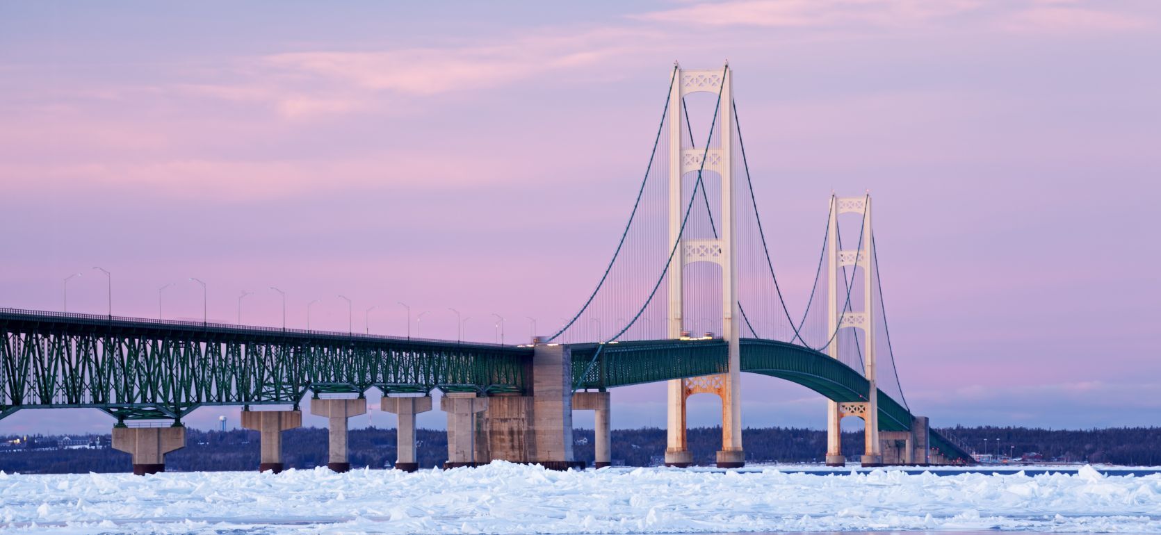 Mackinac Bridge with a sunset in the background and ice in the foreground.