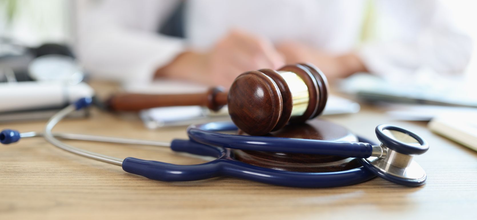 Judge hammer and a stethoscope on a desk with a doctor in the back.
