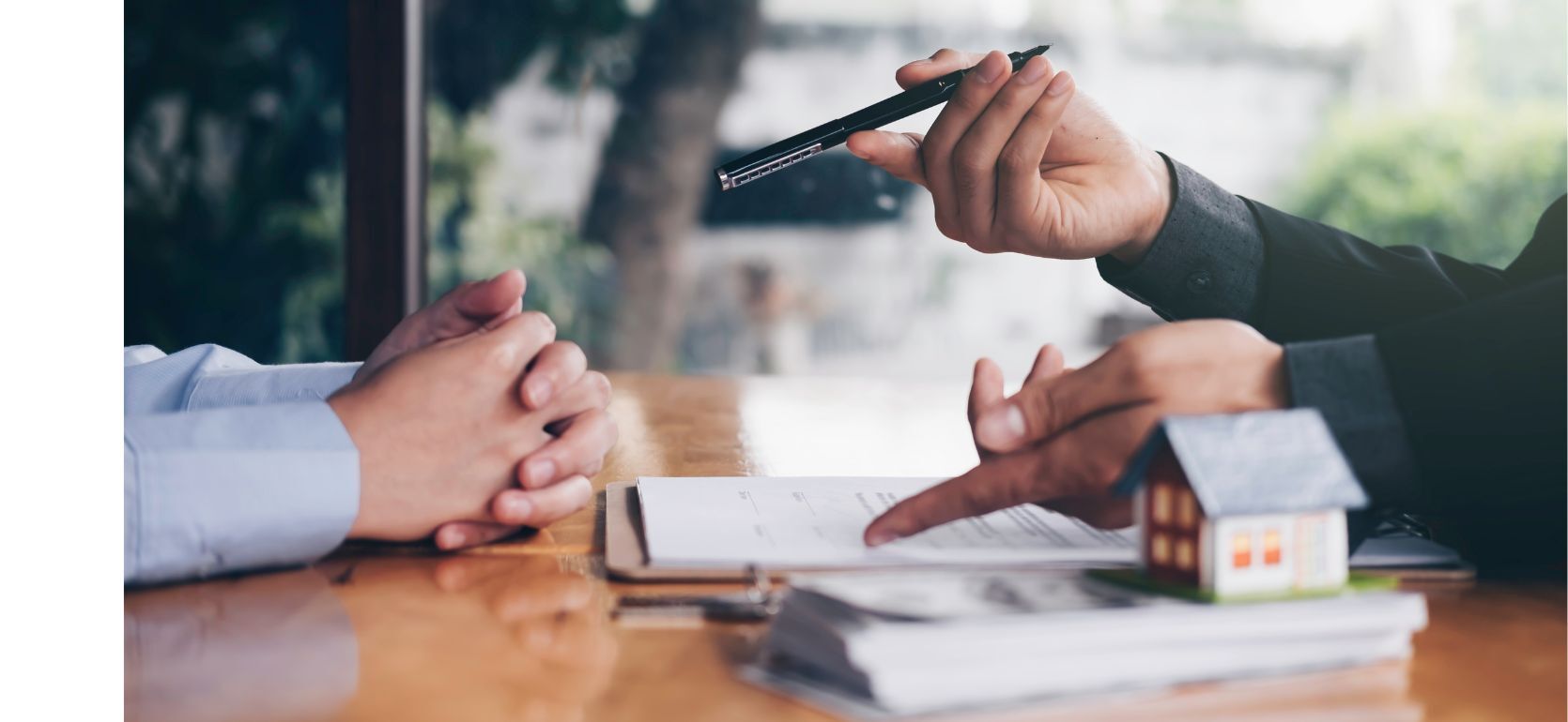 People discussing with a pile of money next to them with a small house model on top.