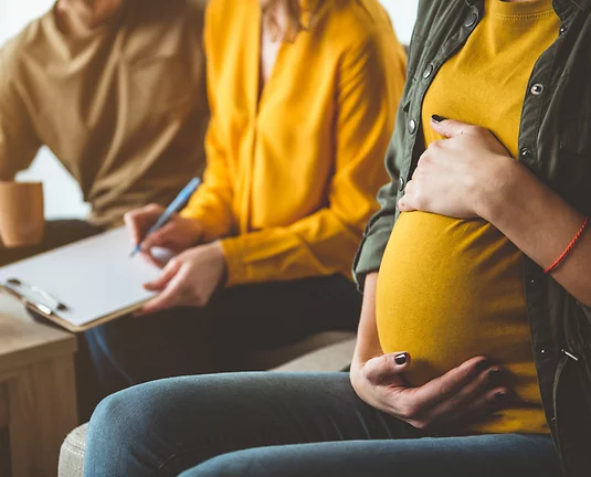 Pregnant women holding her belly sitting next to a couple writing on clipboard