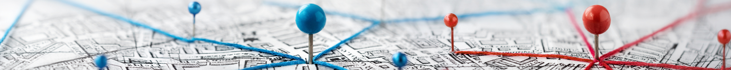 Close-up of a map with blue and red push pins connected by string, marking various locations.