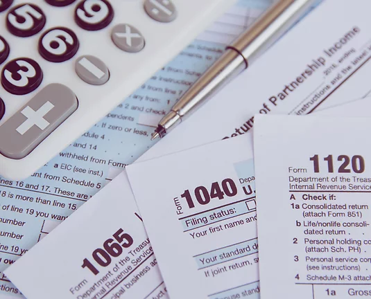 Various tax form papers stacked on each other with pen and calculator laying above.