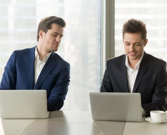 A guy peeking at the laptop next to him.