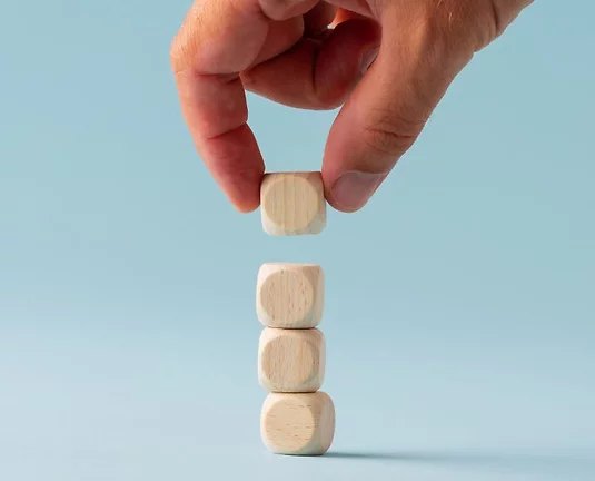 A hand stakcing four wood blocks with a blue background.