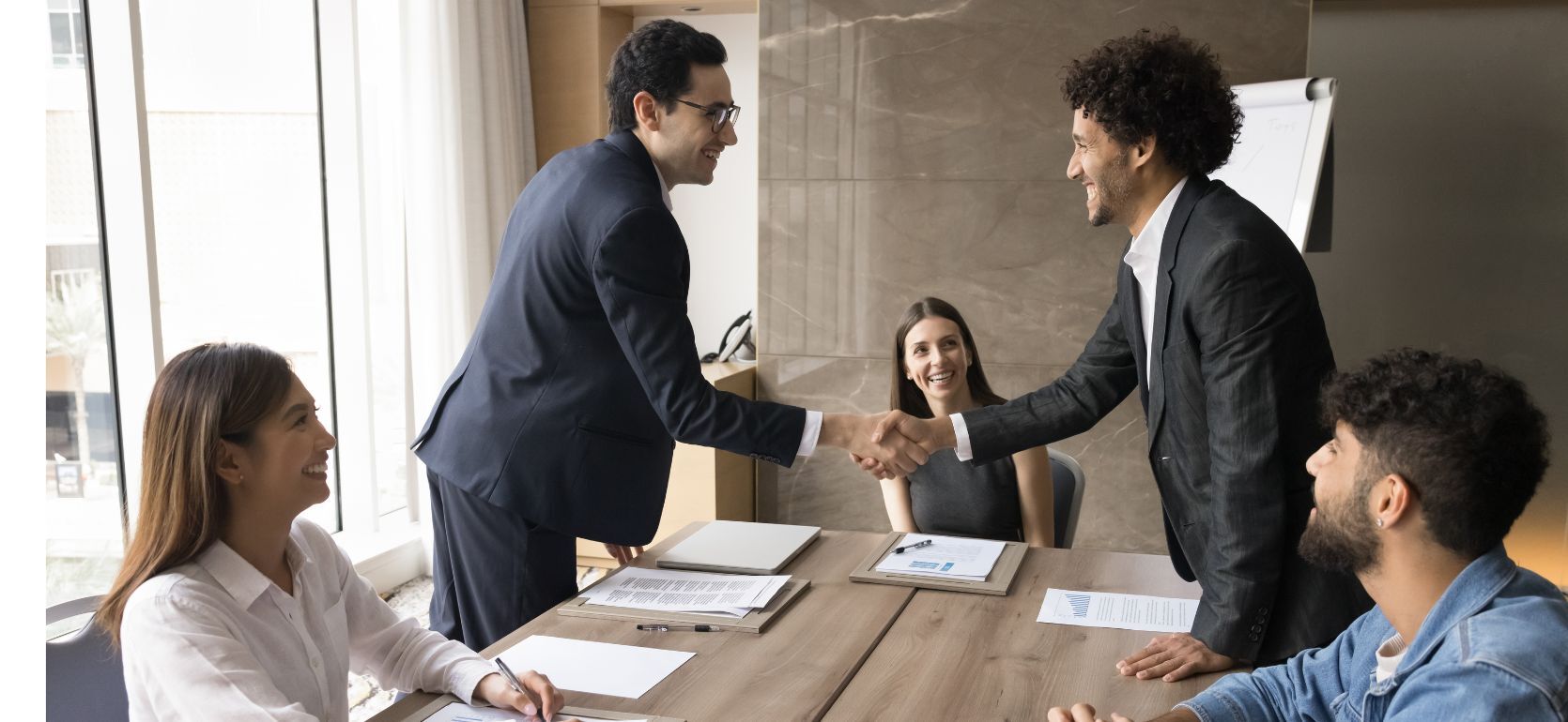Two people shaking hands with three people smiling around them.