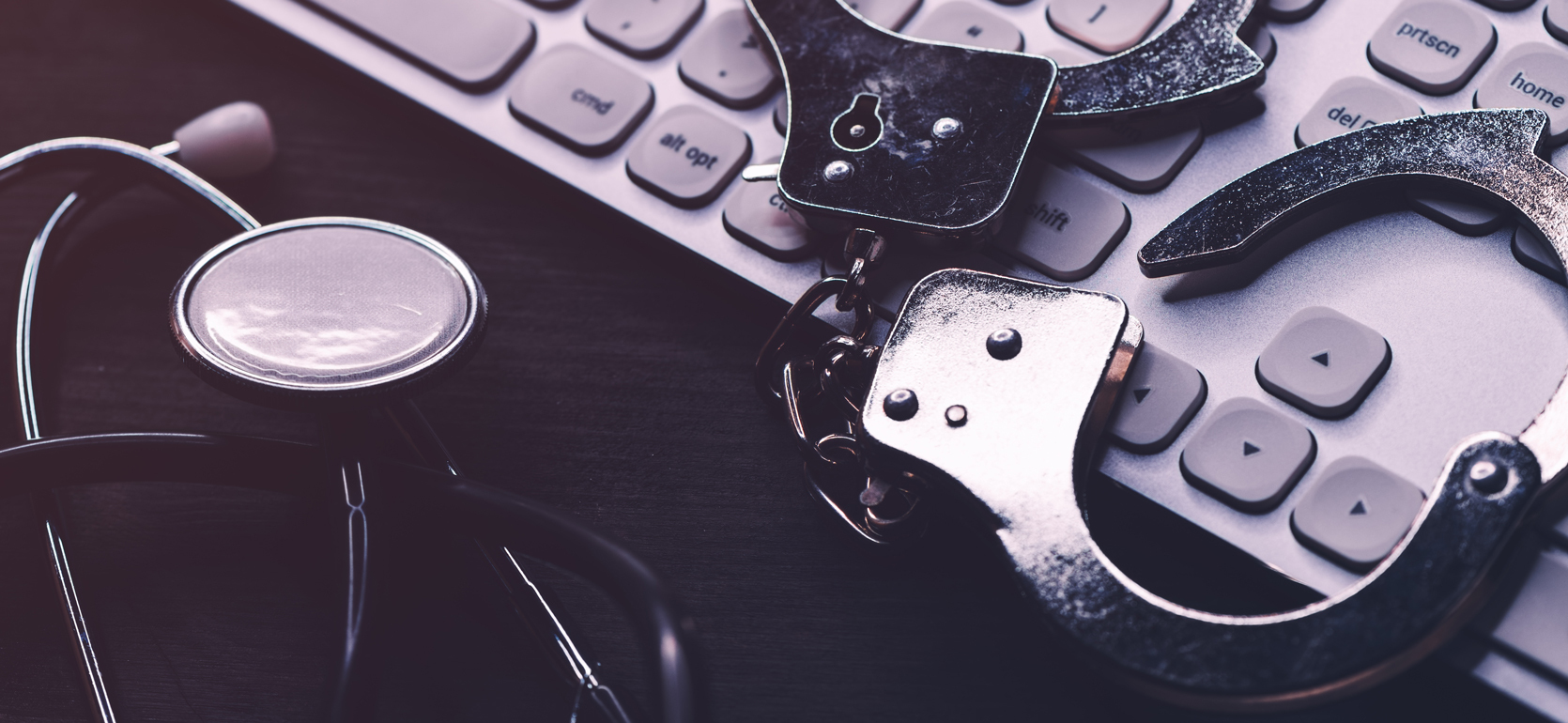 Keyboard with pair of metal handcuffs laying on it with a stethoscope next to it.