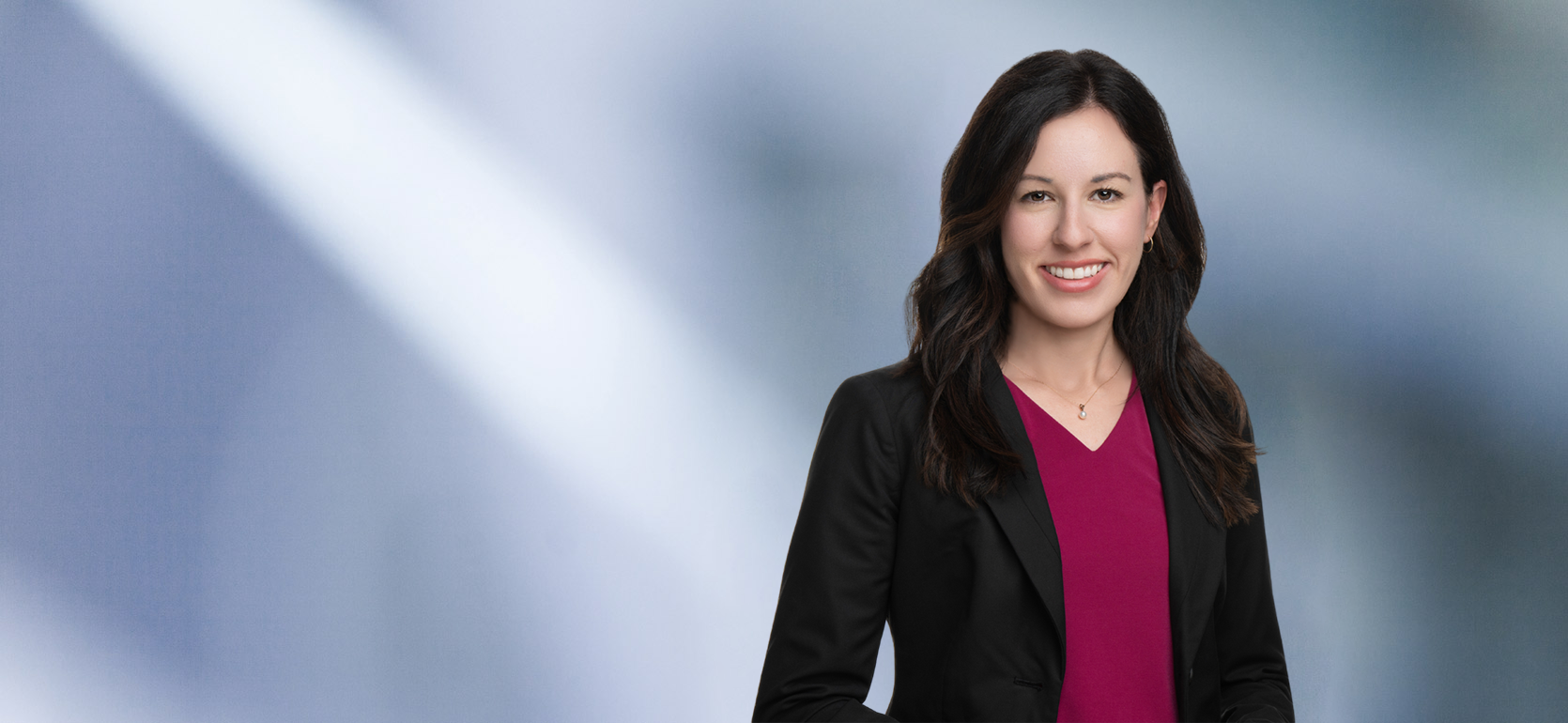 A woman, Julie Hamlet, in a black blazer and purple top is smiling at the camera, standing against a blurred blue and white background.