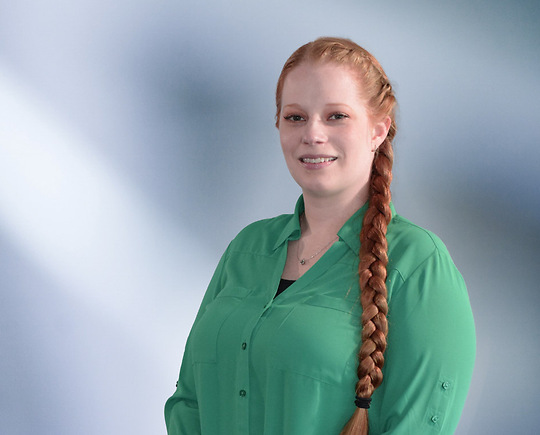 woman, Toni Harris, with shoulder-length blonde hair in a dark blazer, with a blurred blue and white background.