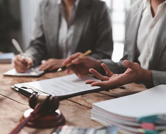 Hands holding pens among contracts, paperwork and gavel