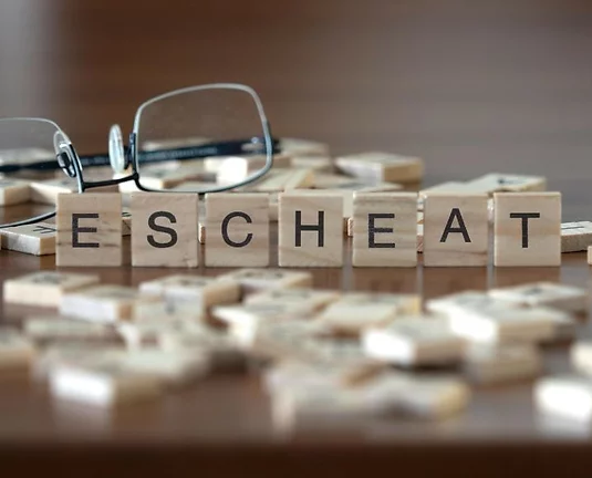 Wooden letter tiles spelling the word "ESCHEAT" on a table, with scattered tiles and a pair of eyeglasses in the background.