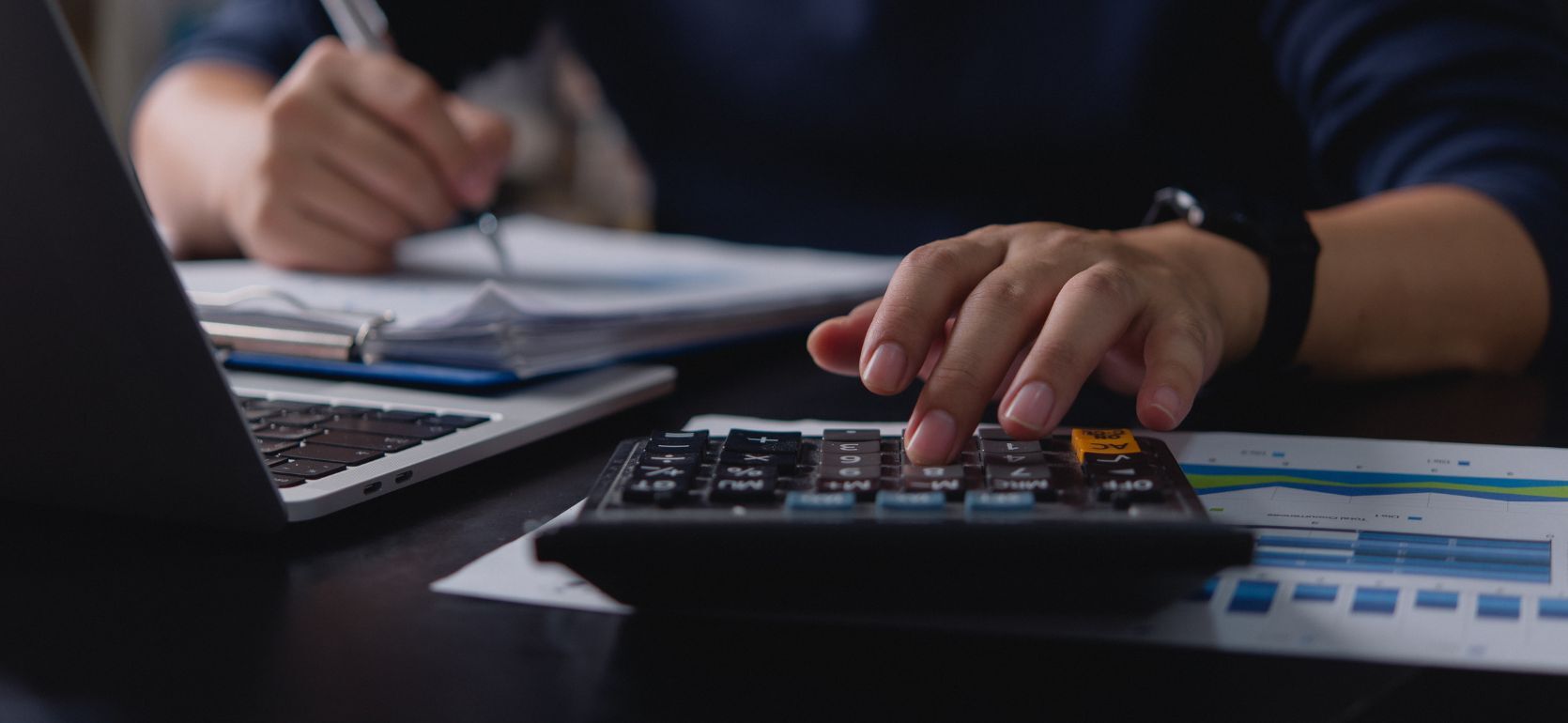 Someone typing on a calculator and writing.