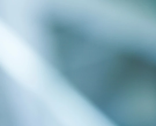 A blurred abstract image featuring soft blue and white tones, possibly showing light reflections or an out-of-focus architectural structure.