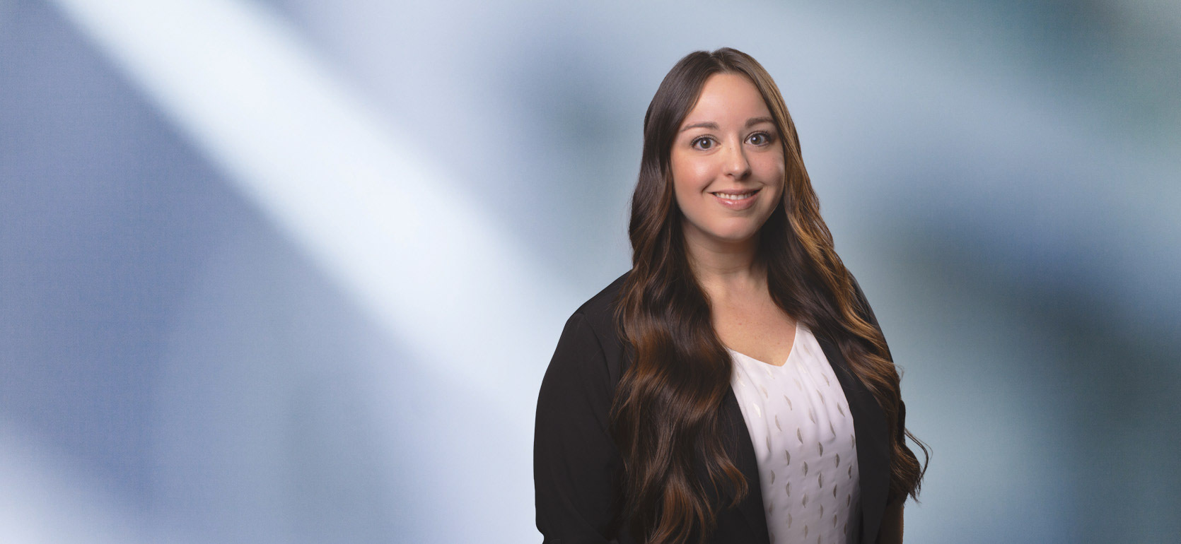 A woman, Shamarr Gearhart, in a dark suit and light blouse is smiling at the camera, standing against a blurred blue and white background.