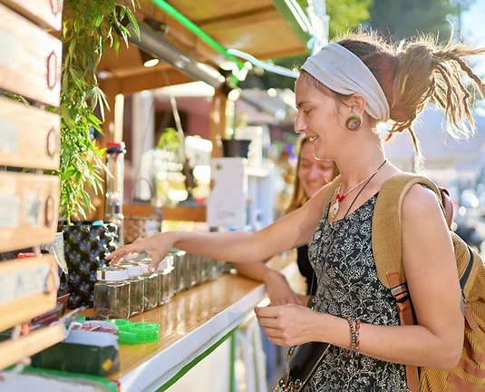 Young women with dreadlocks browse cannabis products at retail stand.