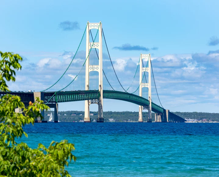 Metal suspension bridge on sunny day stretched over expanse of blue water