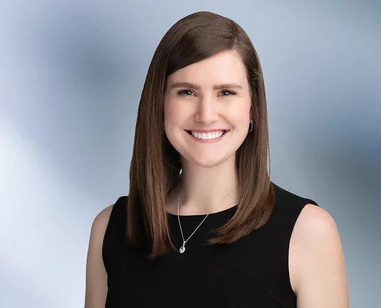Young woman in black dress smiles at camera in front of blue gray background