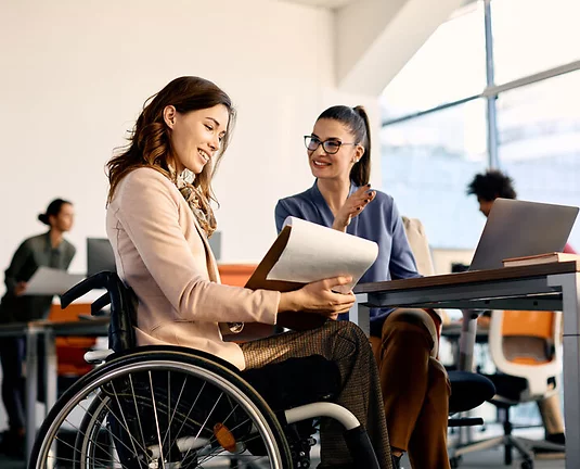 Happy businesswoman in wheelchair going through reports while working female coworker in the office.