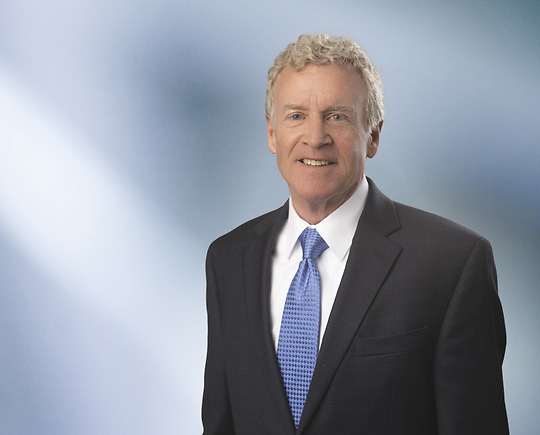 Portrait of a man, Thomas Meagher, with short brown hair in a dark blazer, with a blurred blue and white background.
