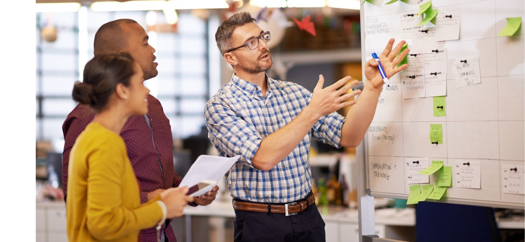 Three people looking a whiteboard filled with sticky notes.