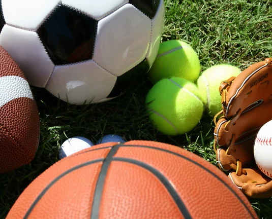 Various sports balls laying on a green grass.