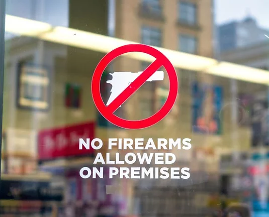 A 'No Firearms Allowed On This Property' sign on a glass door.