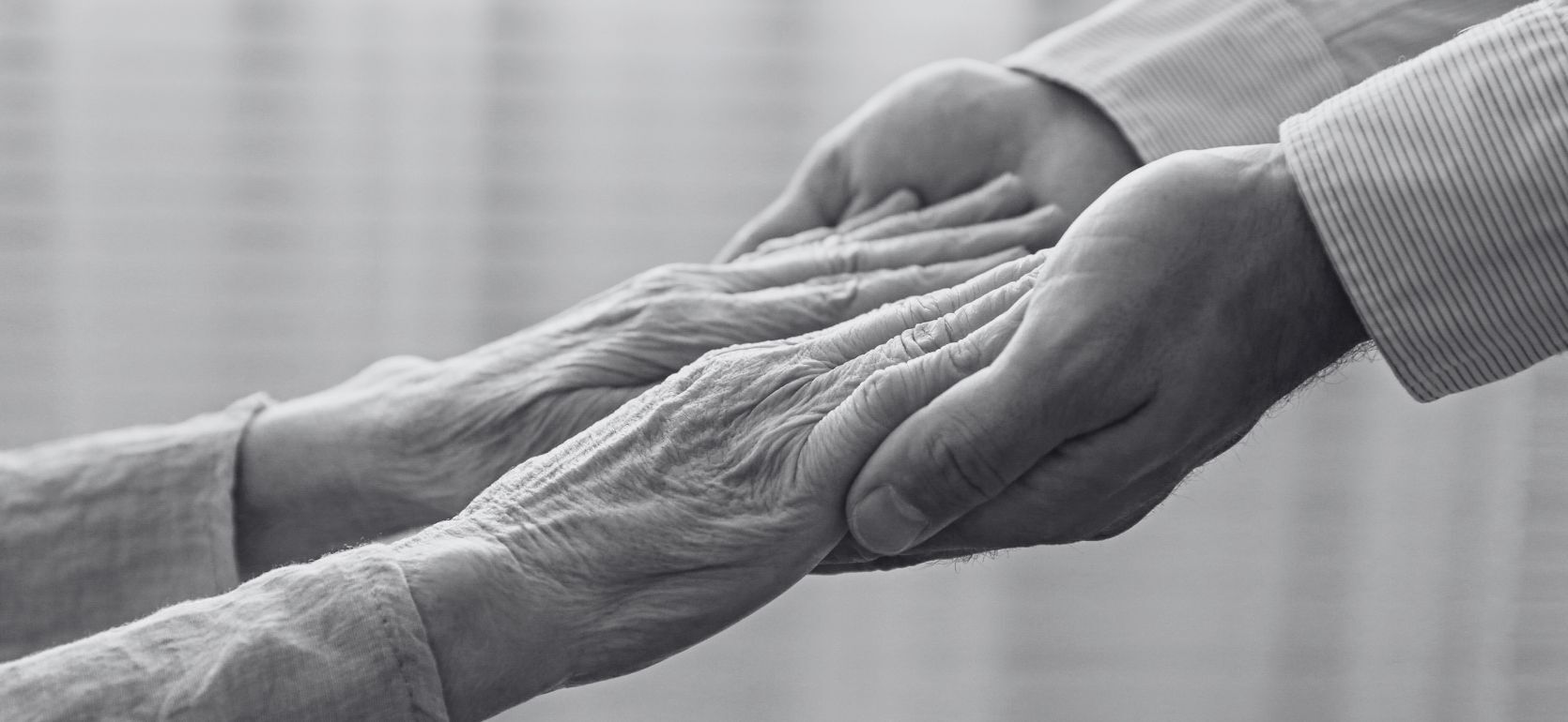 A pair of wrinkled hands holding a pair of unwrinkled hands.