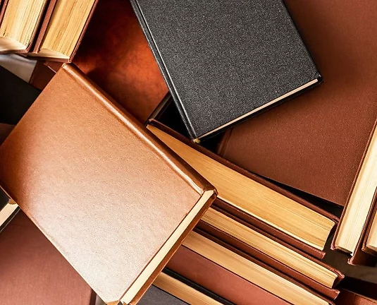 A scattered pile of hardcover books with plain brown and black covers and yellowed pages, viewed from above.