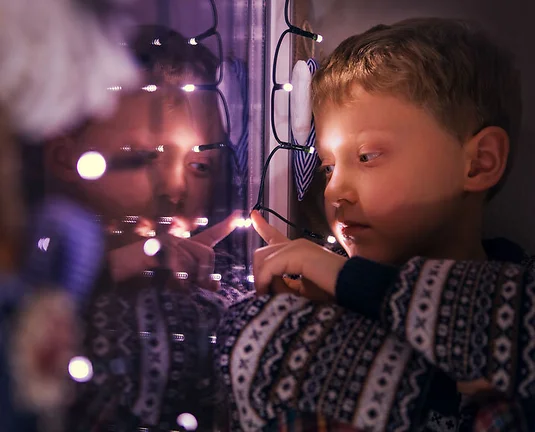 Closeup portrait boy sitting on the window with Christmas Lights