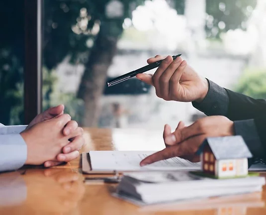 Two people discussing with a pile of money next to them with a small house model on top.