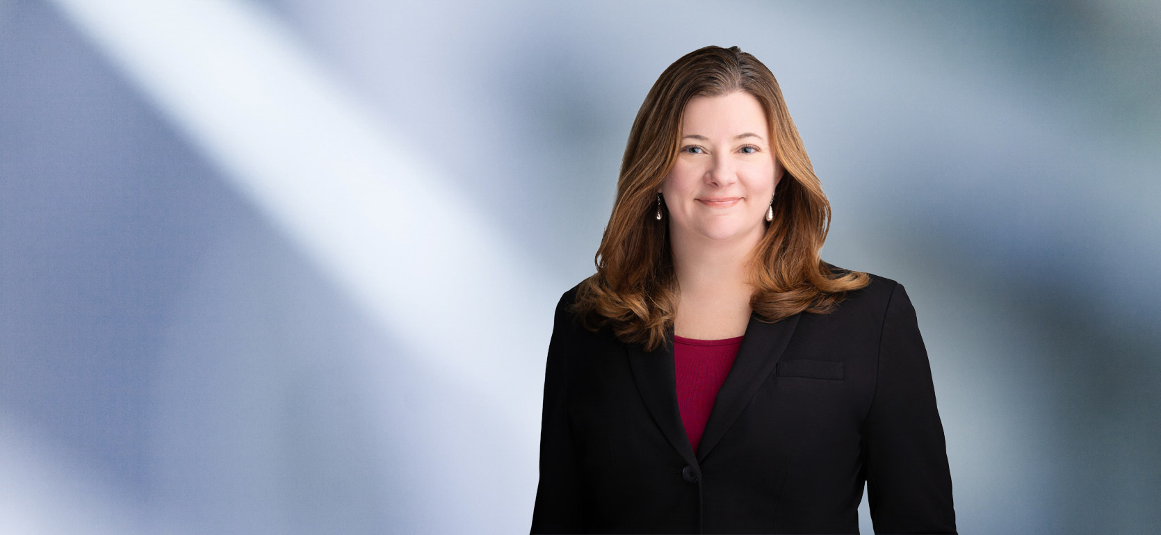woman, Sara Cunningham, with light brown hair, wearing a black blazer, smiling against a blurred blue and white background"