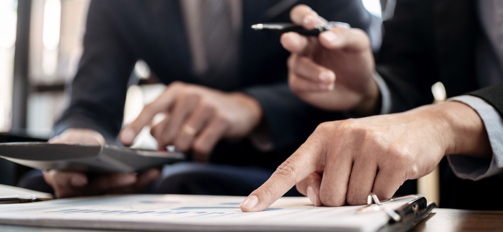 Someone pointing at a paper with graphs on it while holding pen and the person to the left typing on a calucaltor.