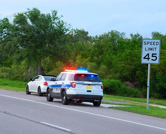 Police truck SUV vehicle with flashing red and blue lights has pulled over a sports car for speeding and they happen to be on the side of the road by a speed limit sign