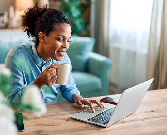 African American Woman Sitting and Holding a Coffee Cup and Scrolling with Other Hand on Laptop