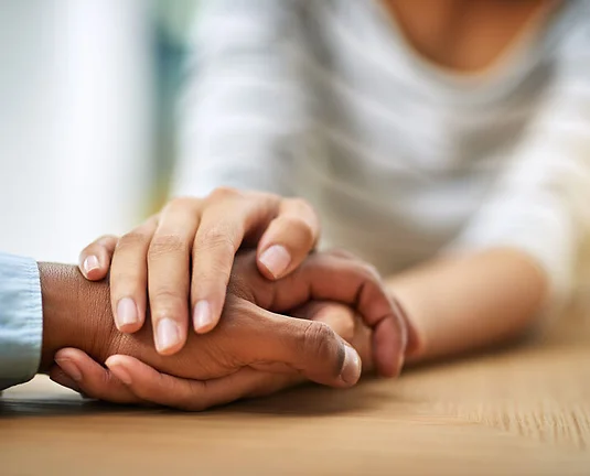 Cropped shot of two unrecognizable people holding hands while being seated at a table inside during the day.