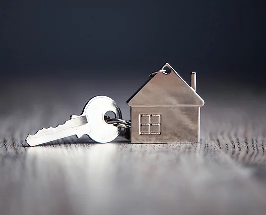 Silver key attached to house shaped keychain on wood tile