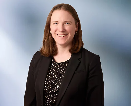 Women smiles at camera wearing black sports jacket with black and gold polka dot blouse.