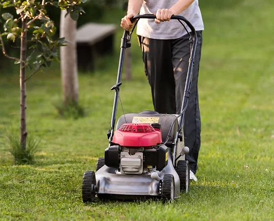 A person pushing a lawn mower across grass.