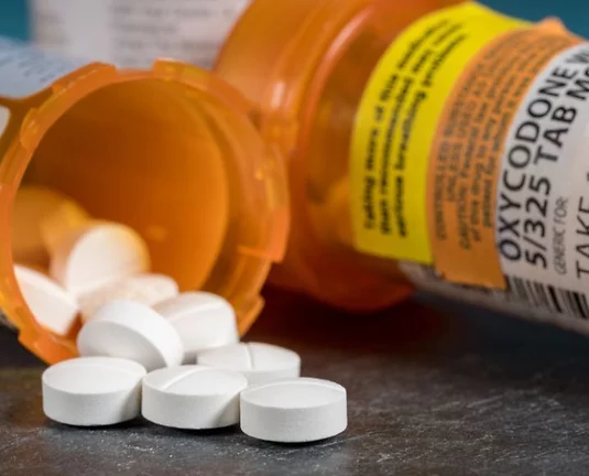 Prescription bottles full of pills. One is tipped over with white tablets spilling out.
