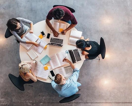 Birds eye view group of 4 college students sitting at a round table covered with homework.