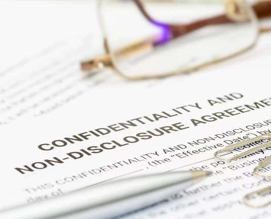 Close-up of a confidentiality and non-disclosure agreement (NDA) document with a pen and eyeglasses resting on top.