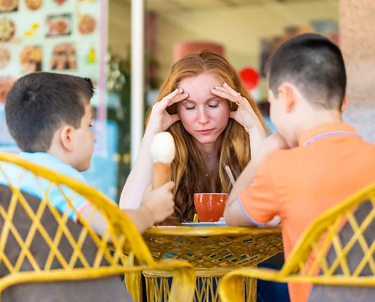 Stressed Mom with her head in her hands sitting in front of two young boys eating ice cream